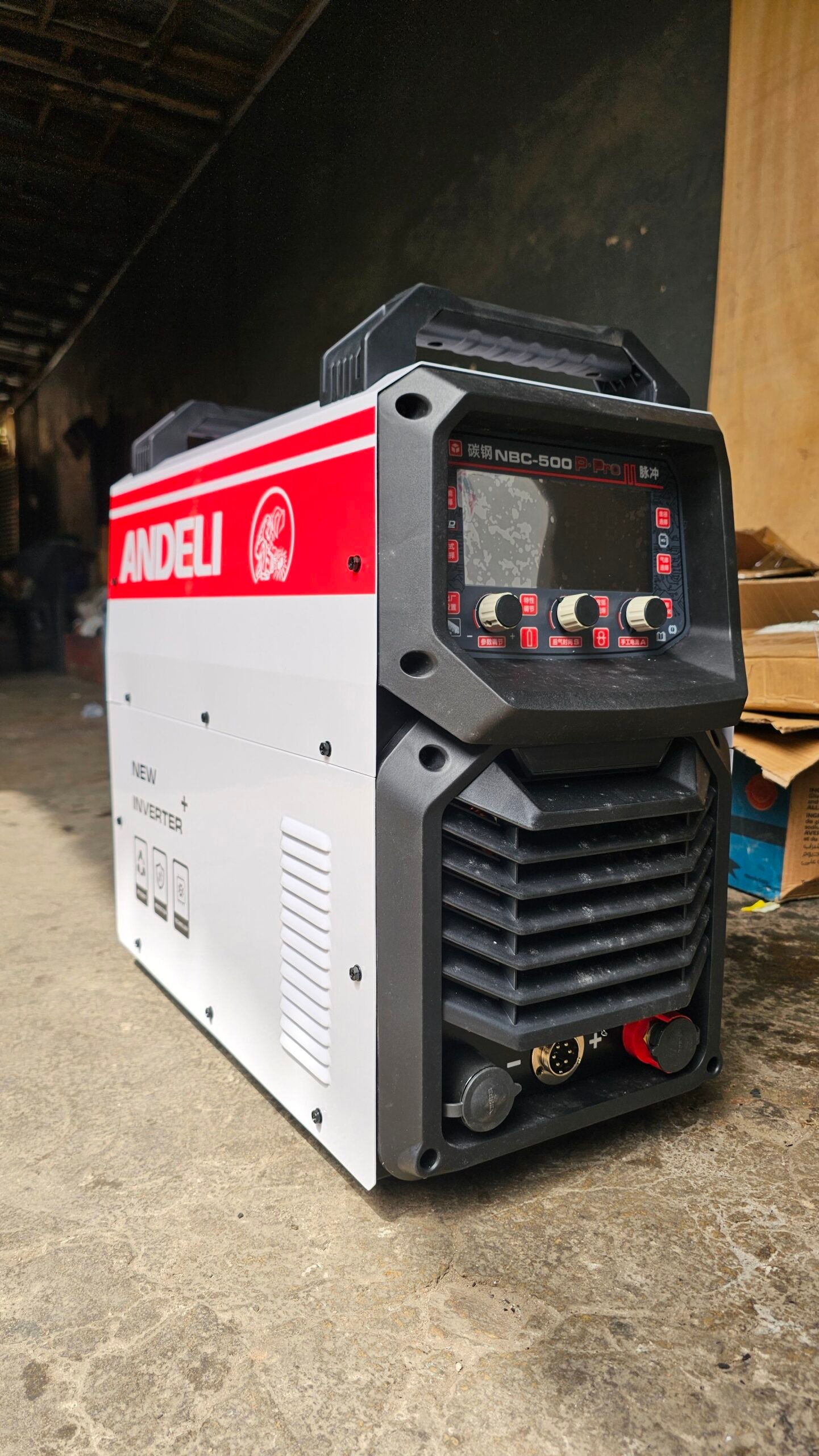 2026/06/1002407398-scaled.jpg - pricemagicgh.com Andeli NBC-500 welding inverter in a workshop, red side panel and control panel with knobs