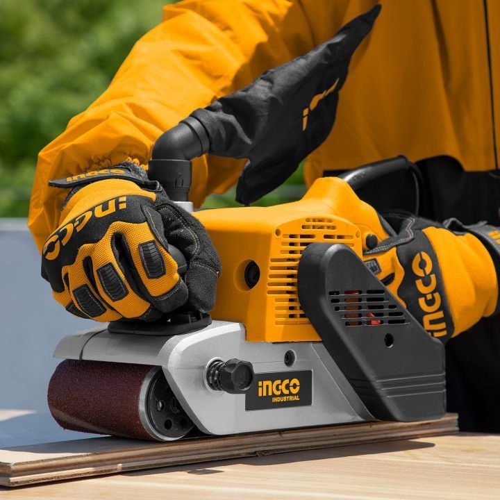2026/06/1002852532.jpg - pricemagicgh.com Worker wearing orange gloves operating a yellow INGCO belt sander on a wooden plank, smoothing the surface.