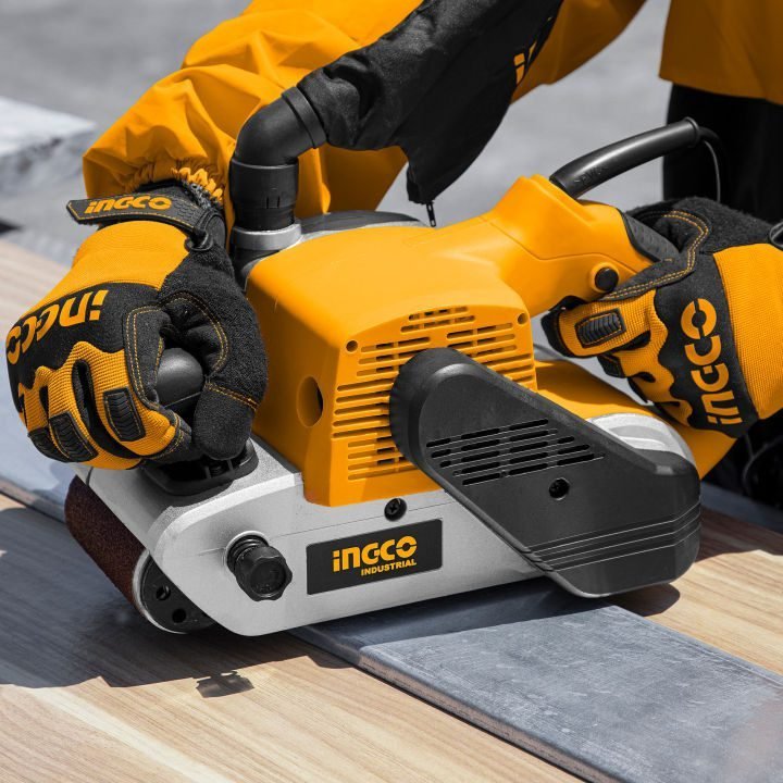 2026/06/1002852533.jpg - pricemagicgh.com Orange Ingco industrial palm sander being operated by gloved hands on a wooden surface, readying to smooth the edge of a board.