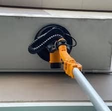 2026/06/1002860489.jpg - pricemagicgh.com Orange power plug connected to a coiled cord entering a recessed electrical outlet on a gray metal surface, likely powering equipment.