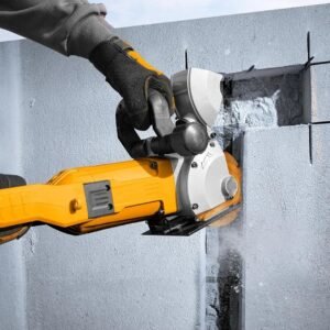 Worker wearing a glove operates a yellow handheld masonry cutter, slicing through concrete blocks with dust spray