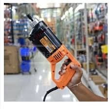 dingqi 10070201 1 - pricemagicgh.com Hand holding an orange heat gun in a hardware store aisle with shelves in the background.