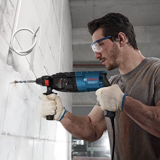 2026101003441204jpg pricemagicghcom Man wearing safety goggles and gloves drilling into a white concrete wall with a blue corded drill